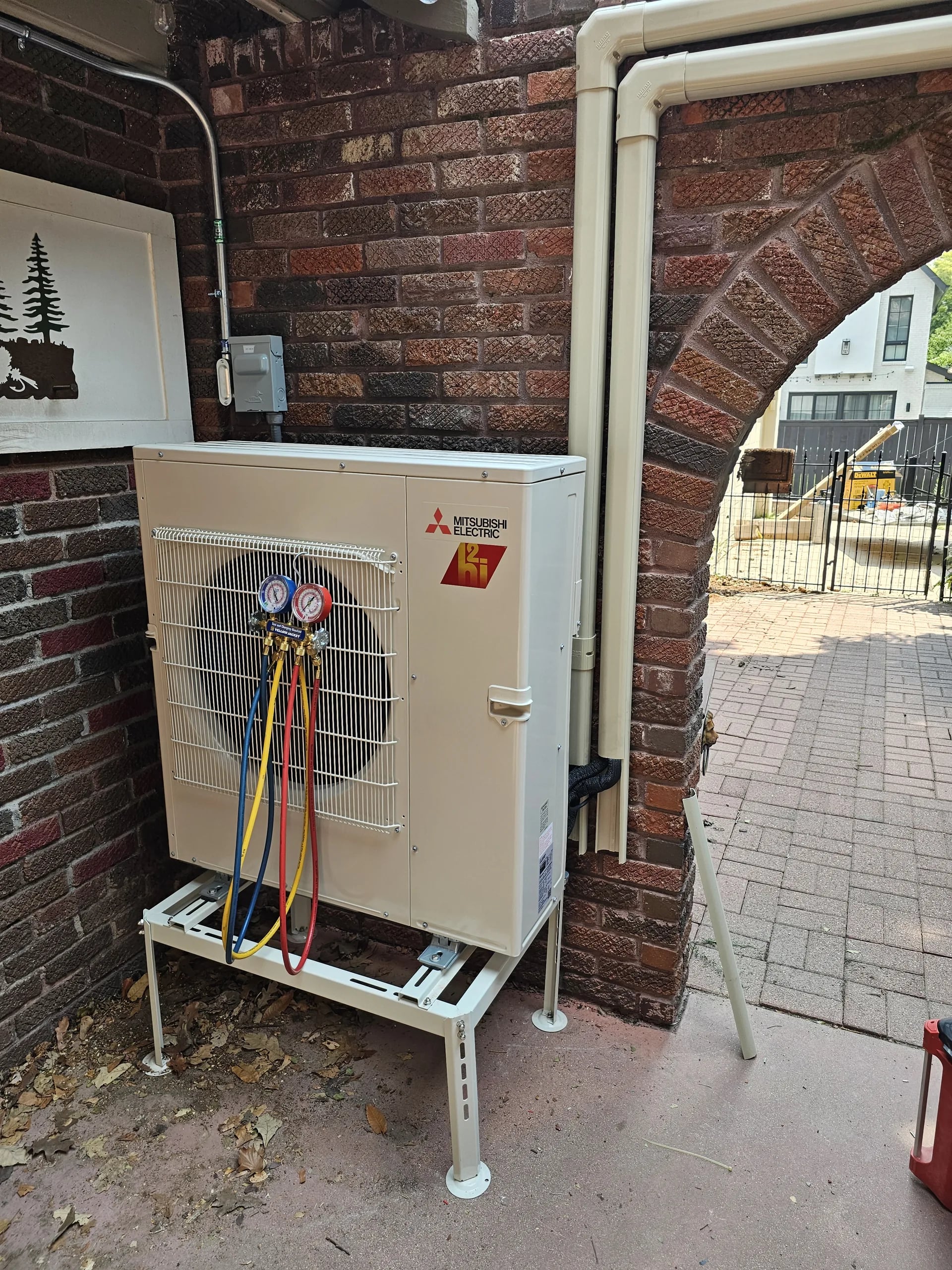Mitsubishi outdoor unit on a stand with refrigerant gauges attached, disconnect on the brick above
