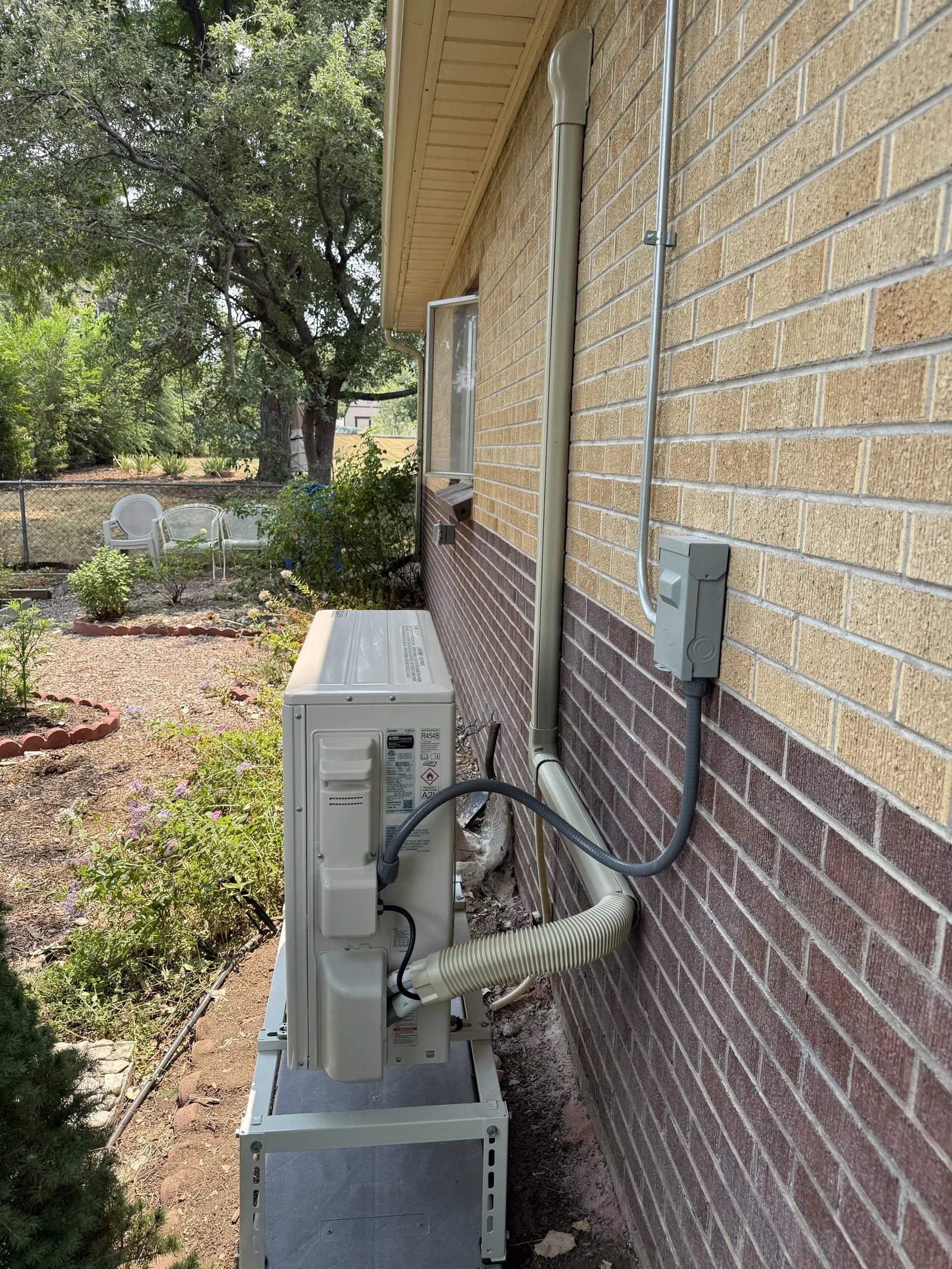 A ductless outdoor unit on a raised stand, with a line-set cover running along a brick wall