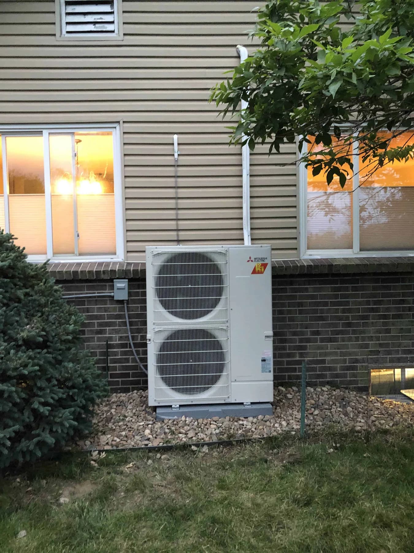 Outdoor heat pump on a wall bracket beside its disconnect and a narrow side yard