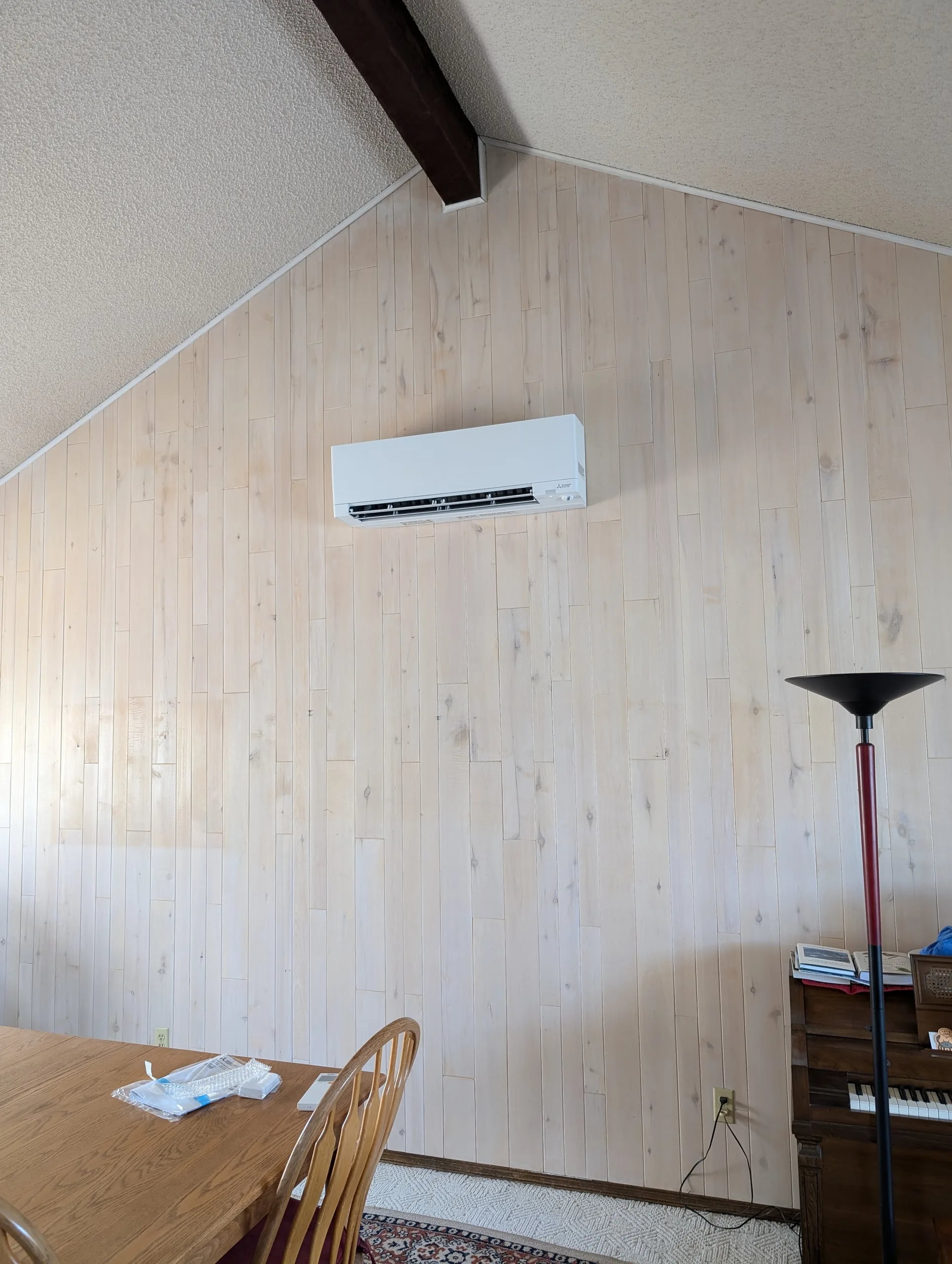Wall-mount mini-split high on a whitewashed plank wall under a vaulted ceiling with an exposed beam